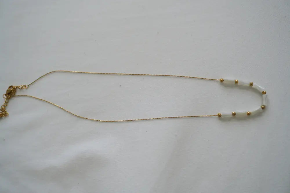 A delicate Mykonos white ceramic and gold beaded chain necklace featuring white cylindrical beads and small golden spheres