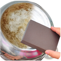 Dark brown rectangular nano emery sponge sanding block held in hand near stainless steel bowl with residue for rust removal