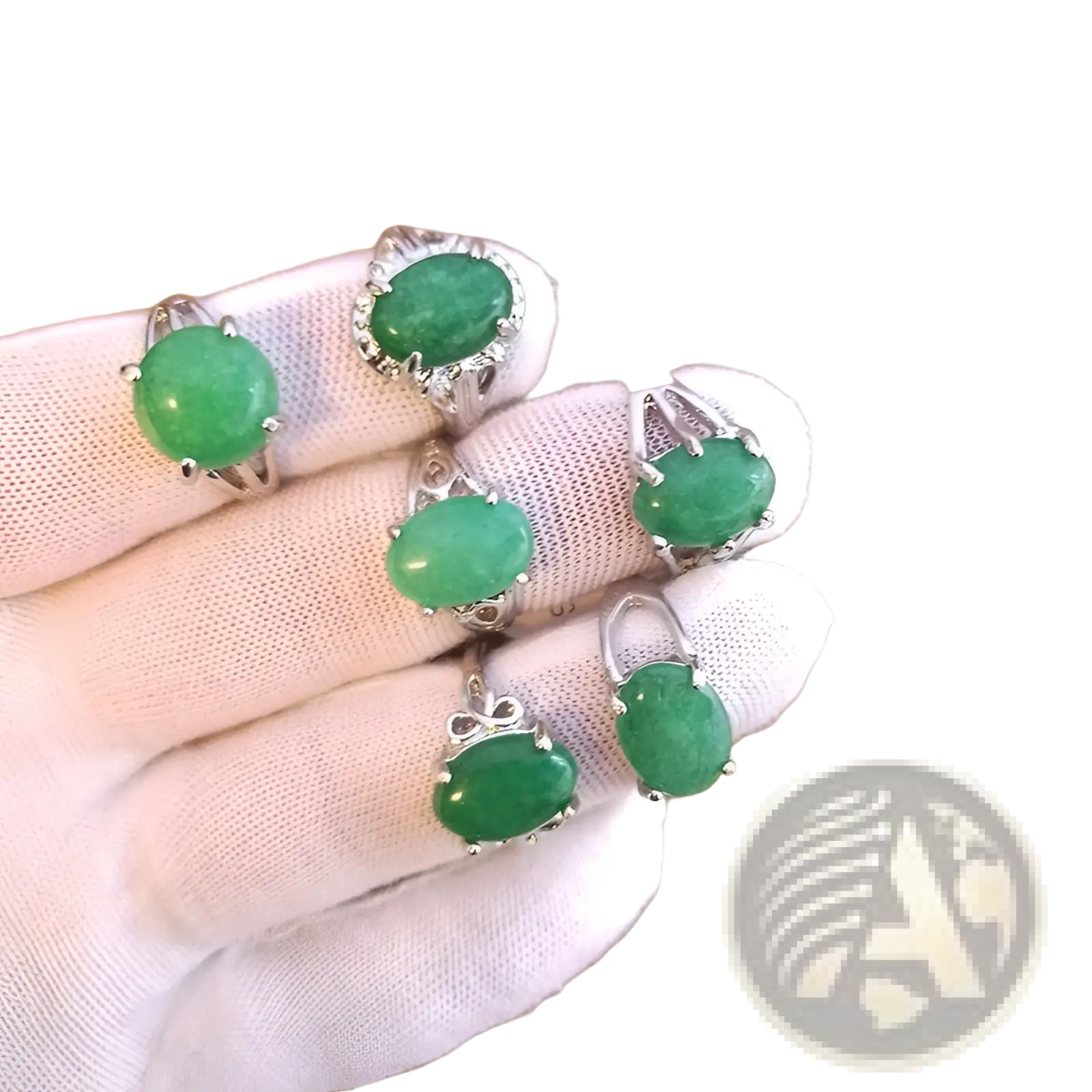 A hand wearing a white glove holds five silver tone statement rings with oval green jade gemstones and intricate filigree