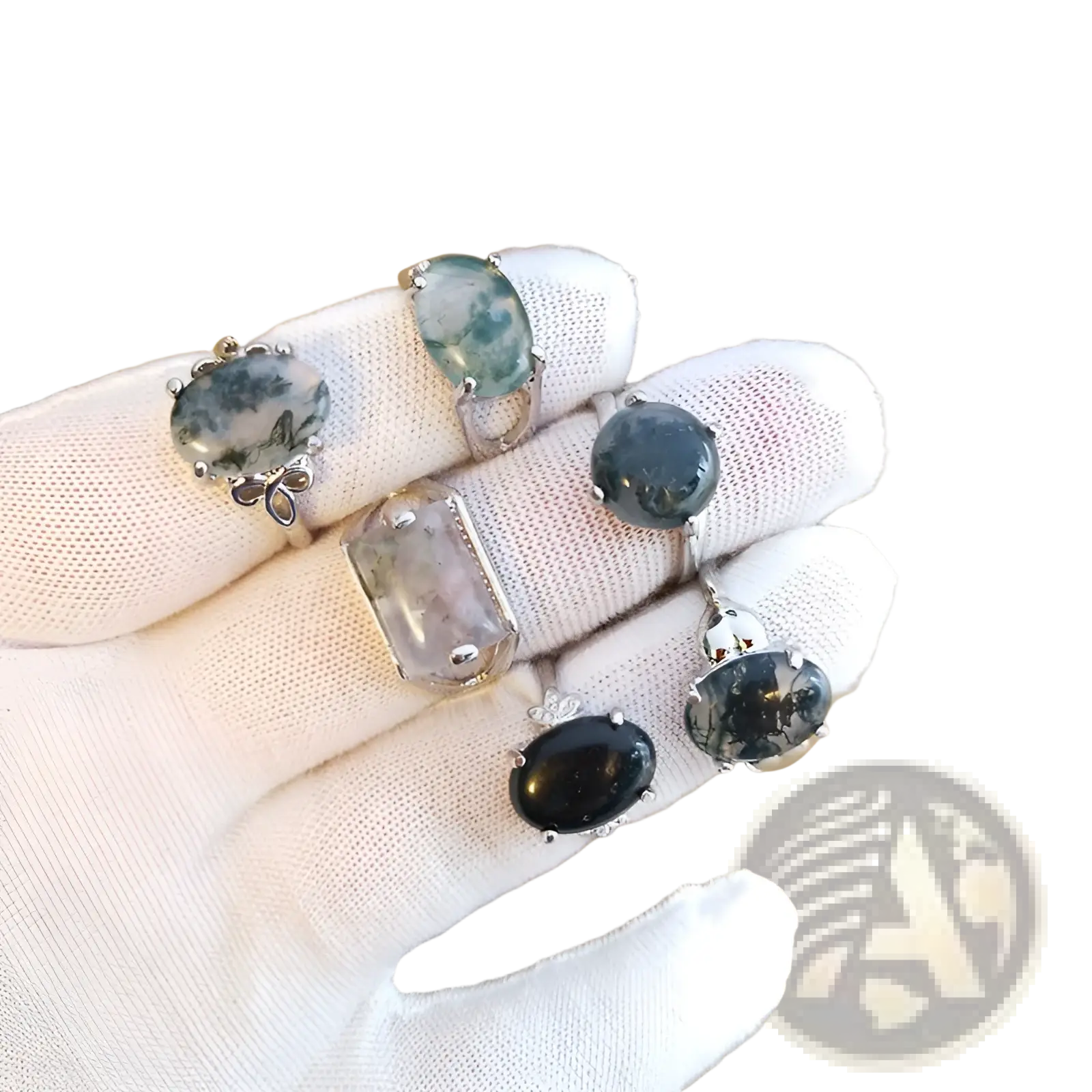 A hand wearing a white glove holds five silver tone statement rings with oval and rectangular moss agate stones