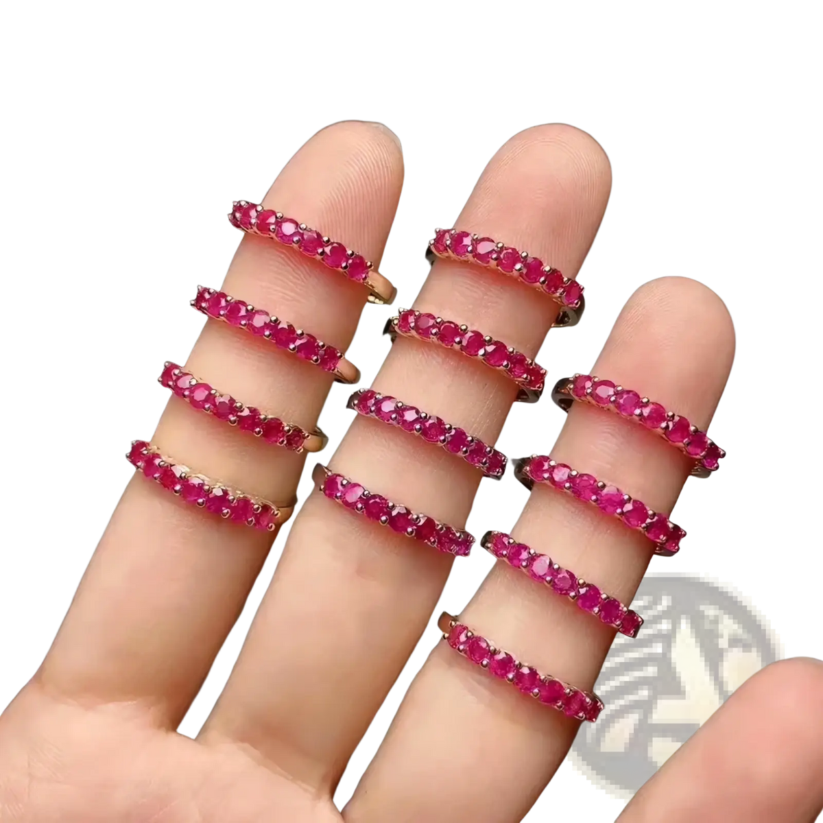 A hand displays multiple delicate rose gold natural ruby silver ring bands with continuous vibrant red rubies