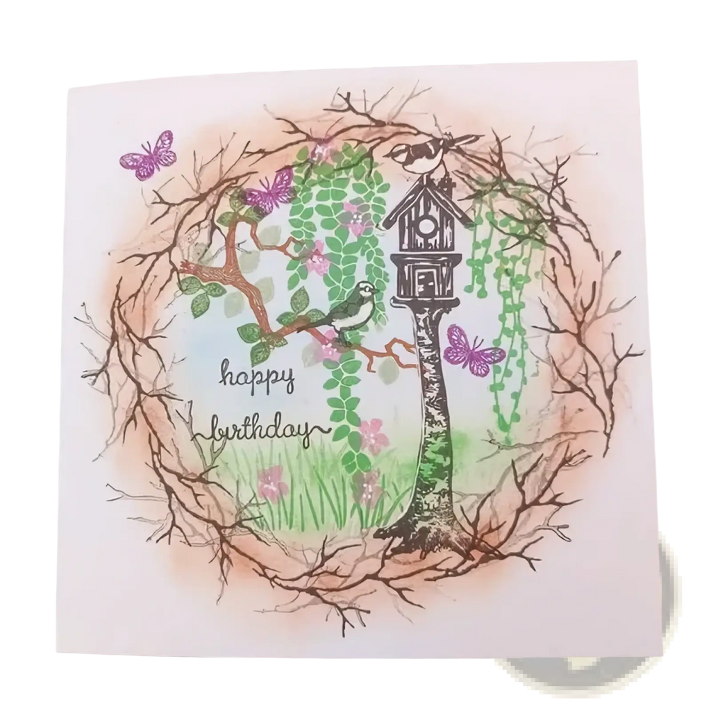 A handcrafted birthday card with a birdhouse surrounded by green vines, pink blossoms, and purple butterflies from nature forest clear stamp set