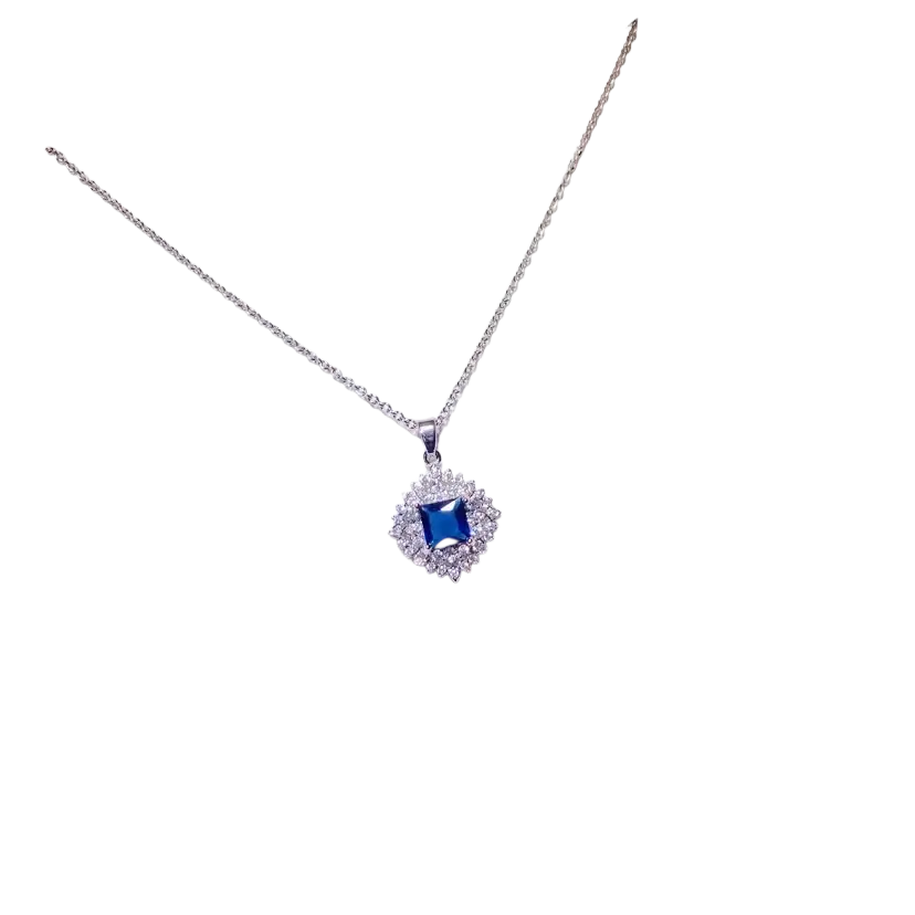 A delicate silver necklace pendant with a square created sapphire gemstone surrounded by clear stones on white card