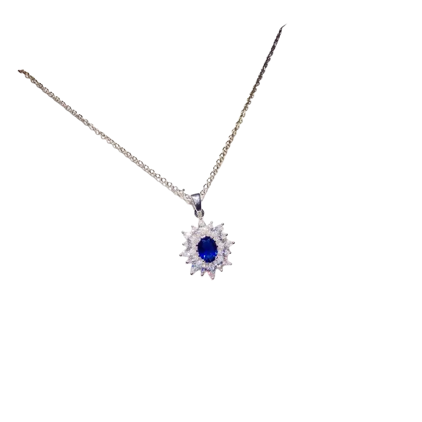 A delicate silver necklace pendant with a central created sapphire surrounded by clear crystals on a white card