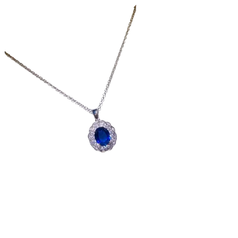A silver necklace pendant with a created sapphire blue gemstone and clear crystal halo on a white card fine jewelry