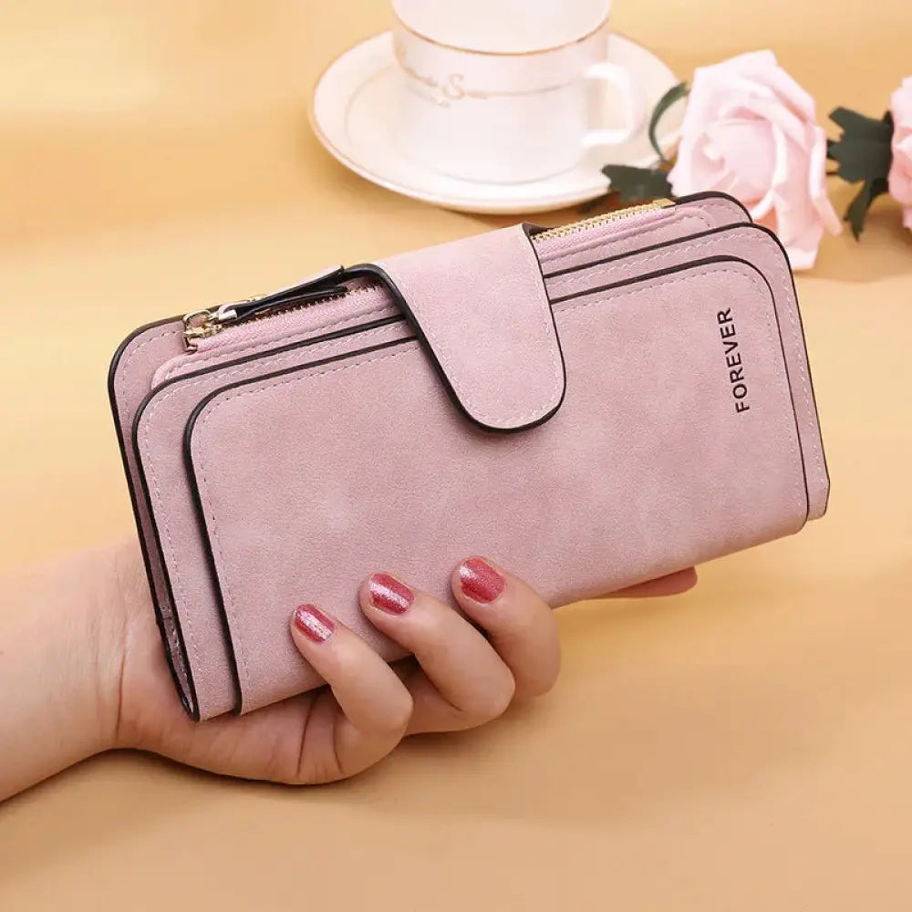 A soft pink suede women’s forever trifold buckle wallet with black trim, gold zipper, and forever embossed on side