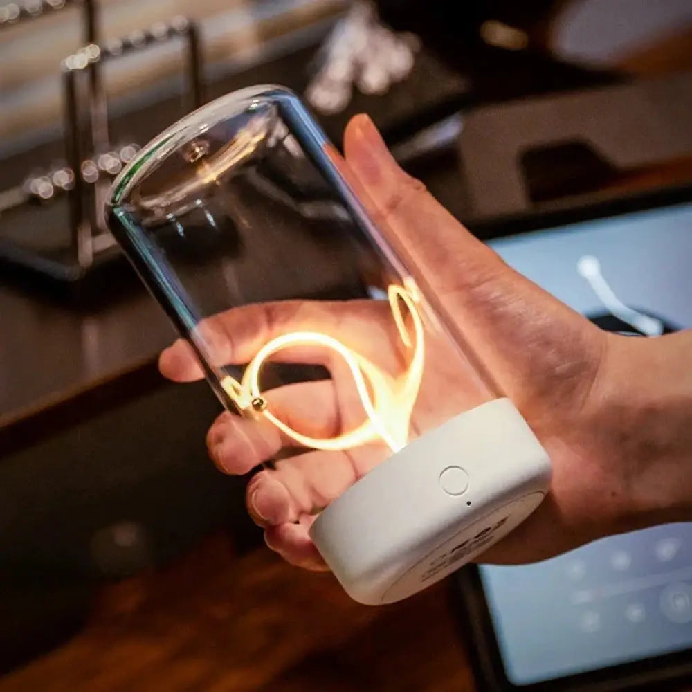A sleek transparent glass rechargeable led filament camping lantern with white base and illuminated gold cord inside