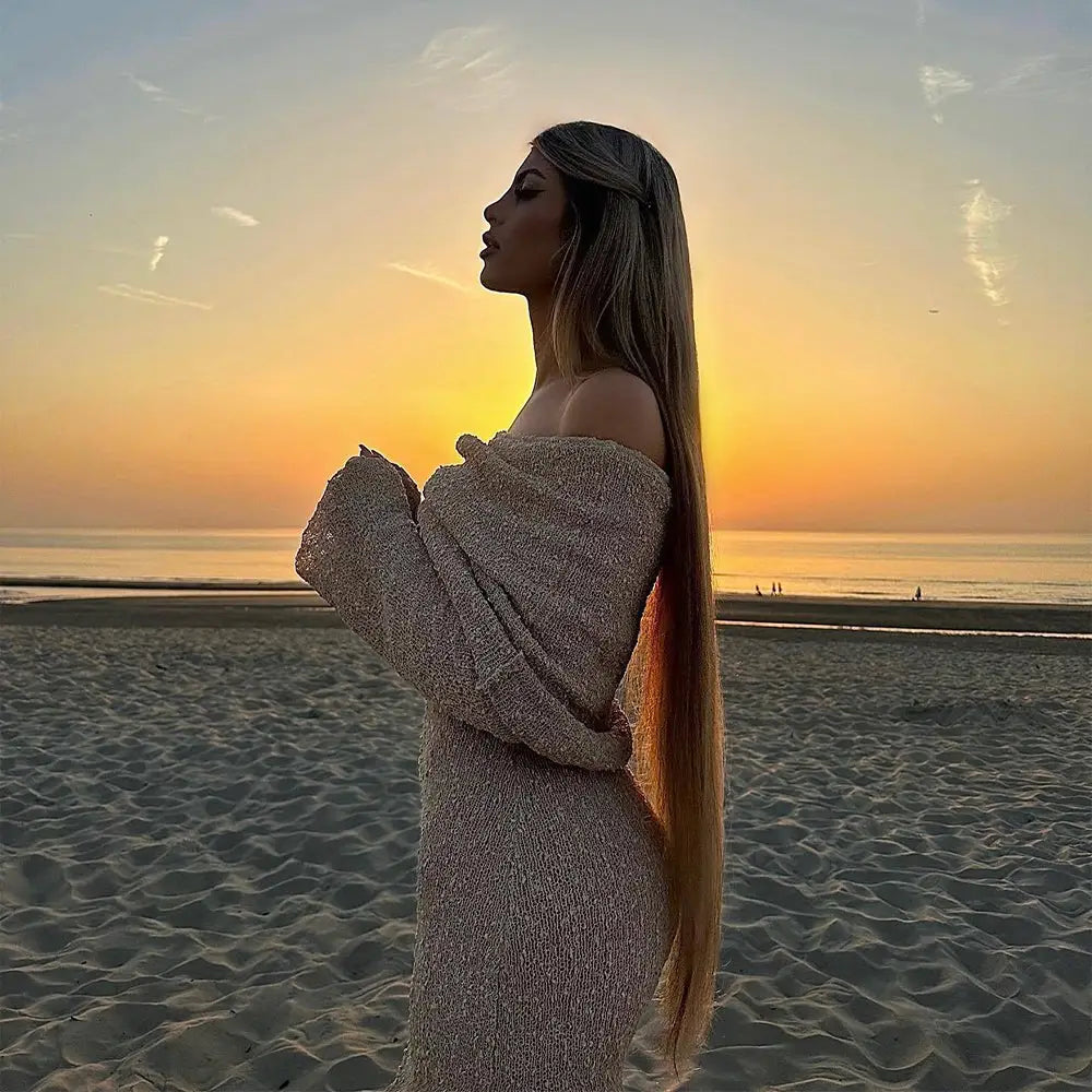 A shimmering off-the-shoulder knit maxi beach dress in soft beige with long sleeves and textured fabric catching sunset light