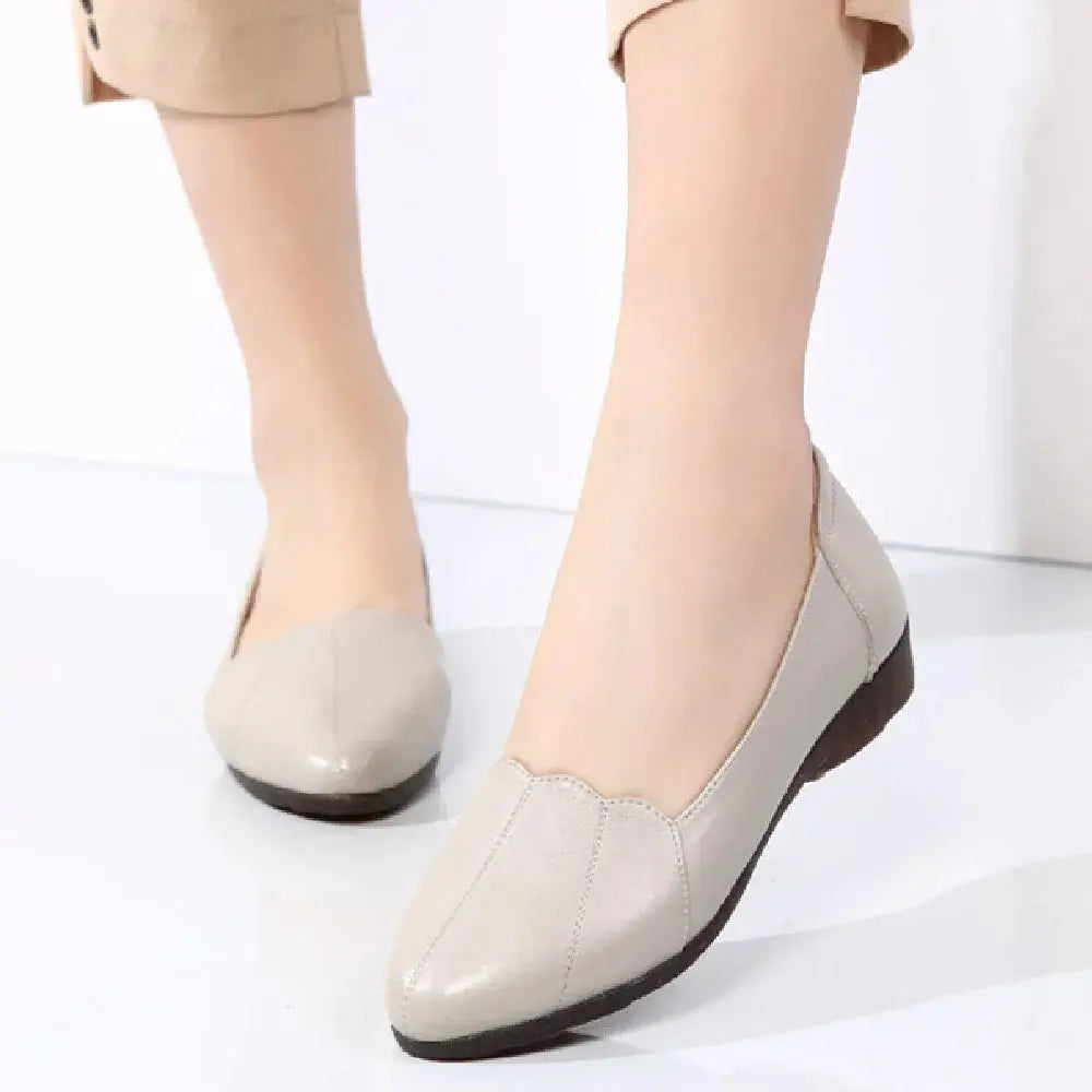 Beige leather flat shoes with scalloped toe design and black rubber soles featuring soft cushioned support