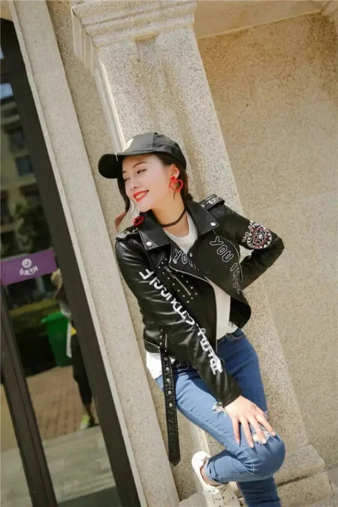 Black faux leather biker jacket with silver studs and white eye embroidered lettering on the back side
