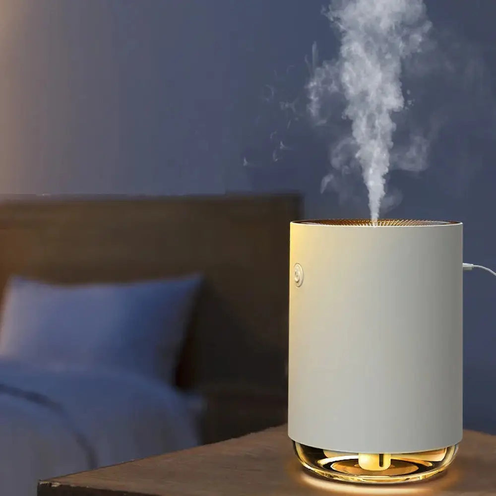 A sleek white cylindrical modern 3-in-1 LED night light and essential oil diffuser with gold accents emitting mist