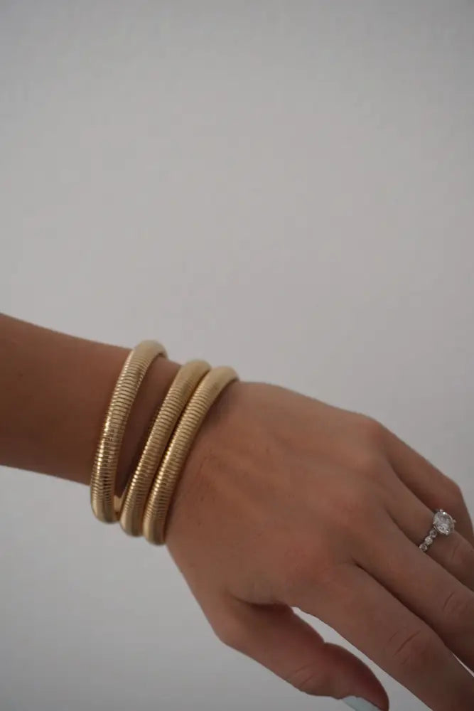 Nova gold ribbed stackable snake bangle bracelets in gold tone worn stacked on a wrist showing front view