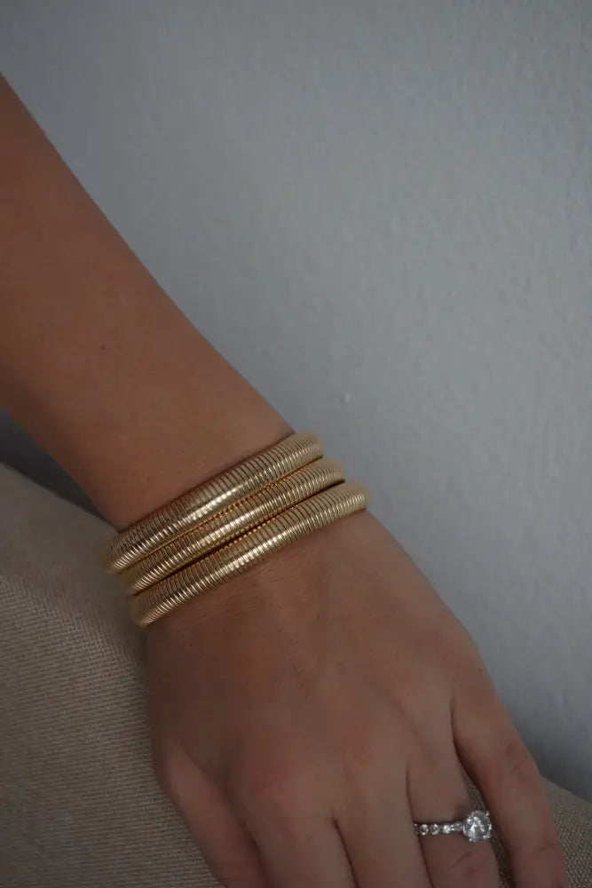 Gold-toned coiled ribbed snake bangle bracelet worn stacked on wrist from nova collection