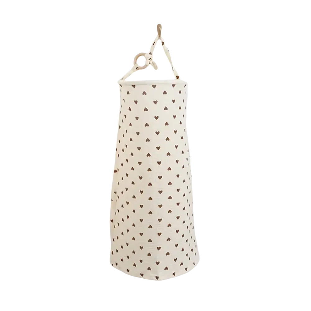 A cream-colored cotton nursing cover storage bag with small brown hearts and a wooden ring handle