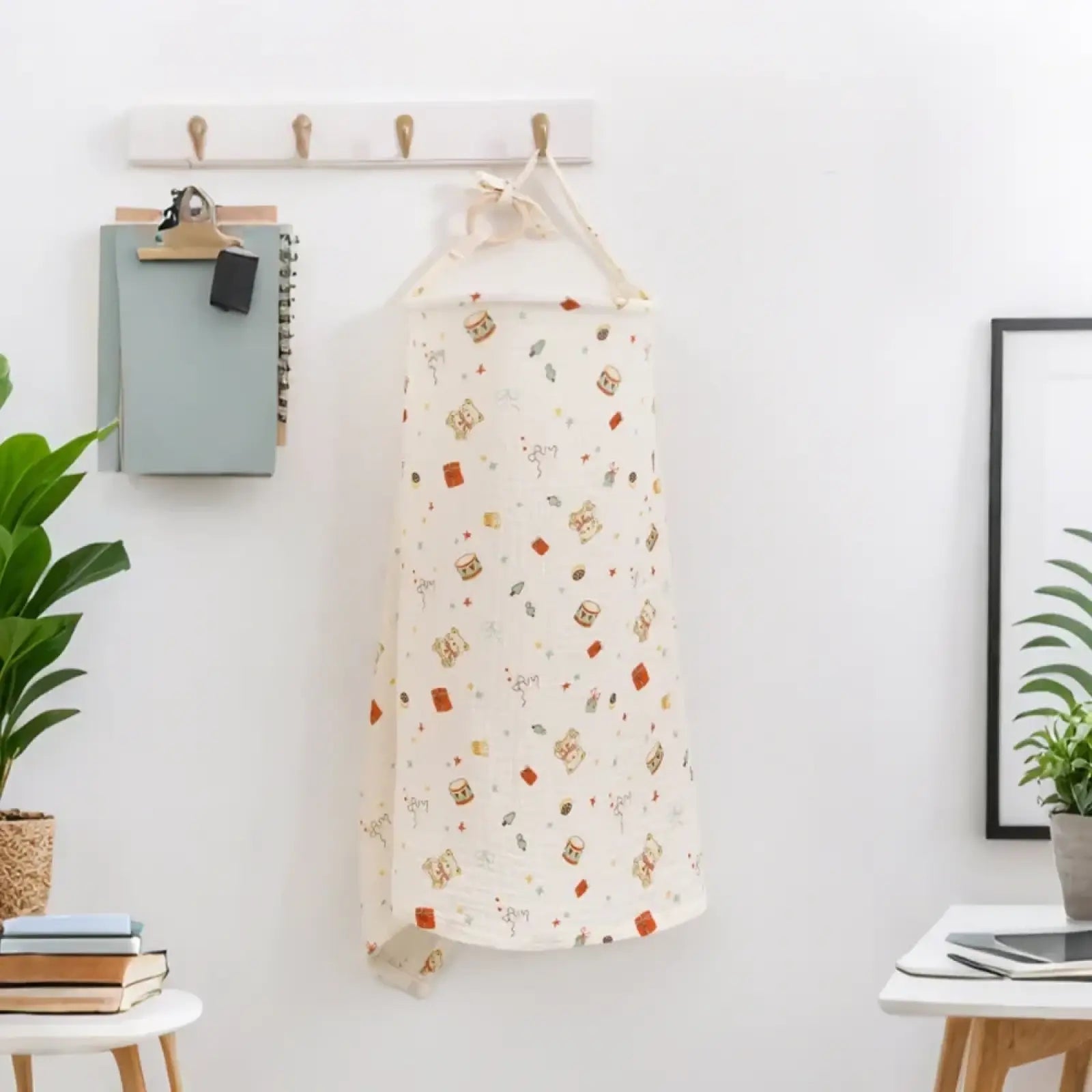 A soft off-white cotton nursing cover with breathable fabric and playful dinosaur print hanging from a wooden hook
