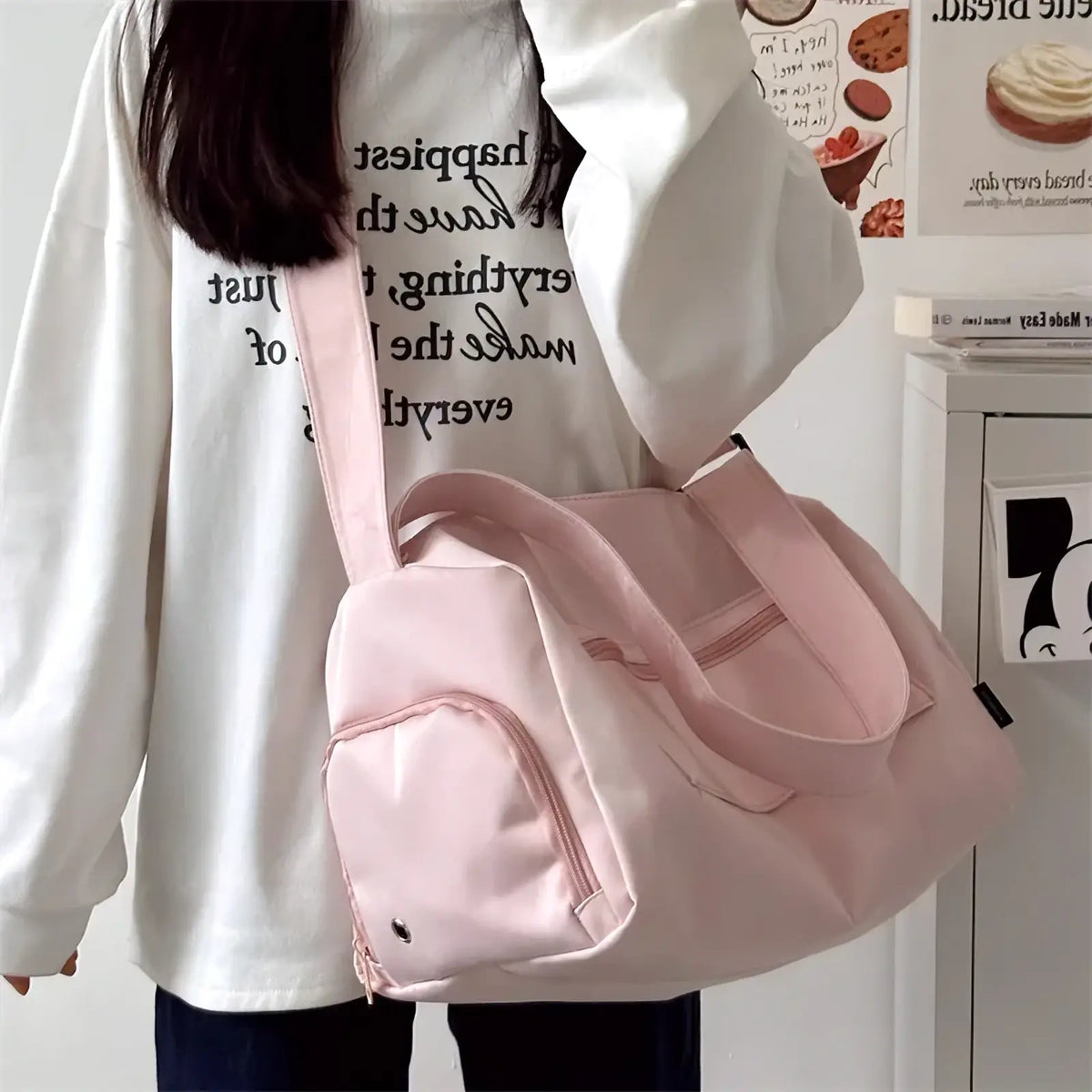 A soft pink nylon travel tote bag with canvas material, matching shoulder strap, and front pocket for casual use