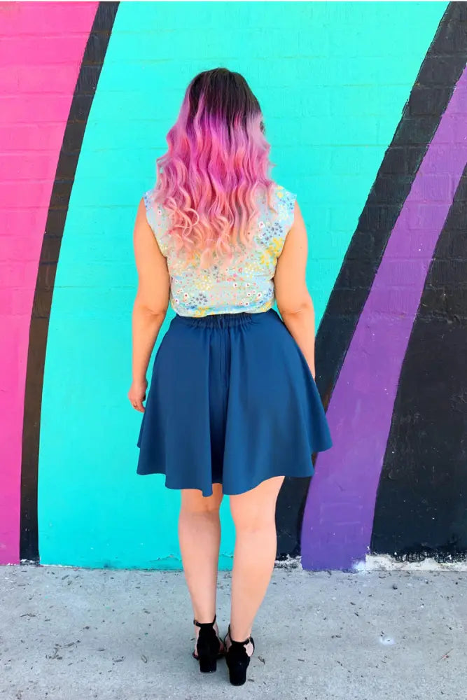 A woman seen from the back wearing an ocean blue high waisted pleated skater skirt with pockets