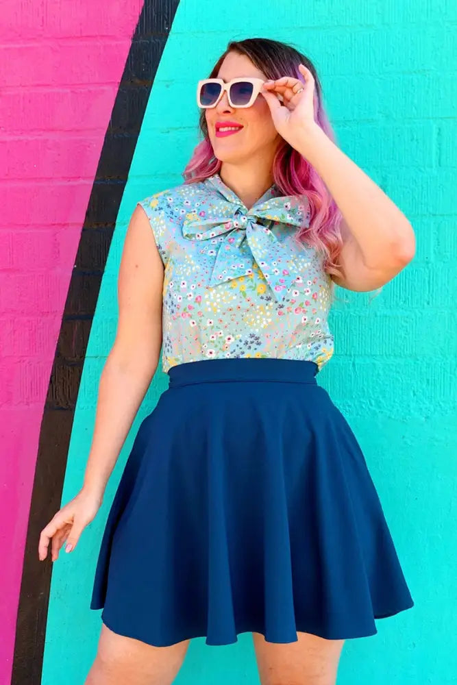 Sleeveless blouse with floral pattern in soft pastel hues and large bow paired with ocean blue high waisted pleated skirt