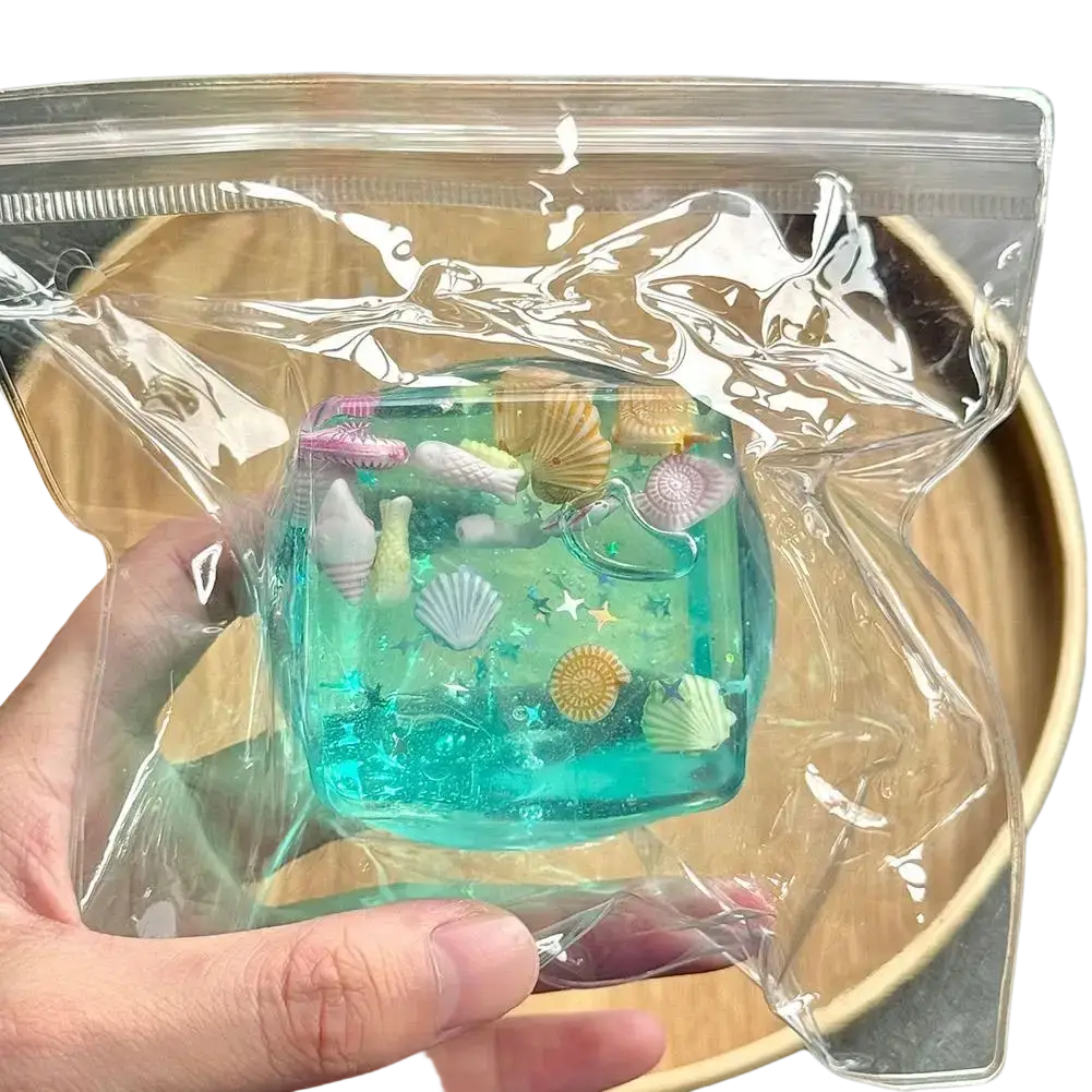 A translucent turquoise resin ocean sensory fidget cube with miniature sea creatures in a clear plastic bag thoughtful gift