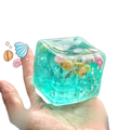 A translucent turquoise fidget toy cube filled with miniature seashells starfish and glittery stars for stress relief