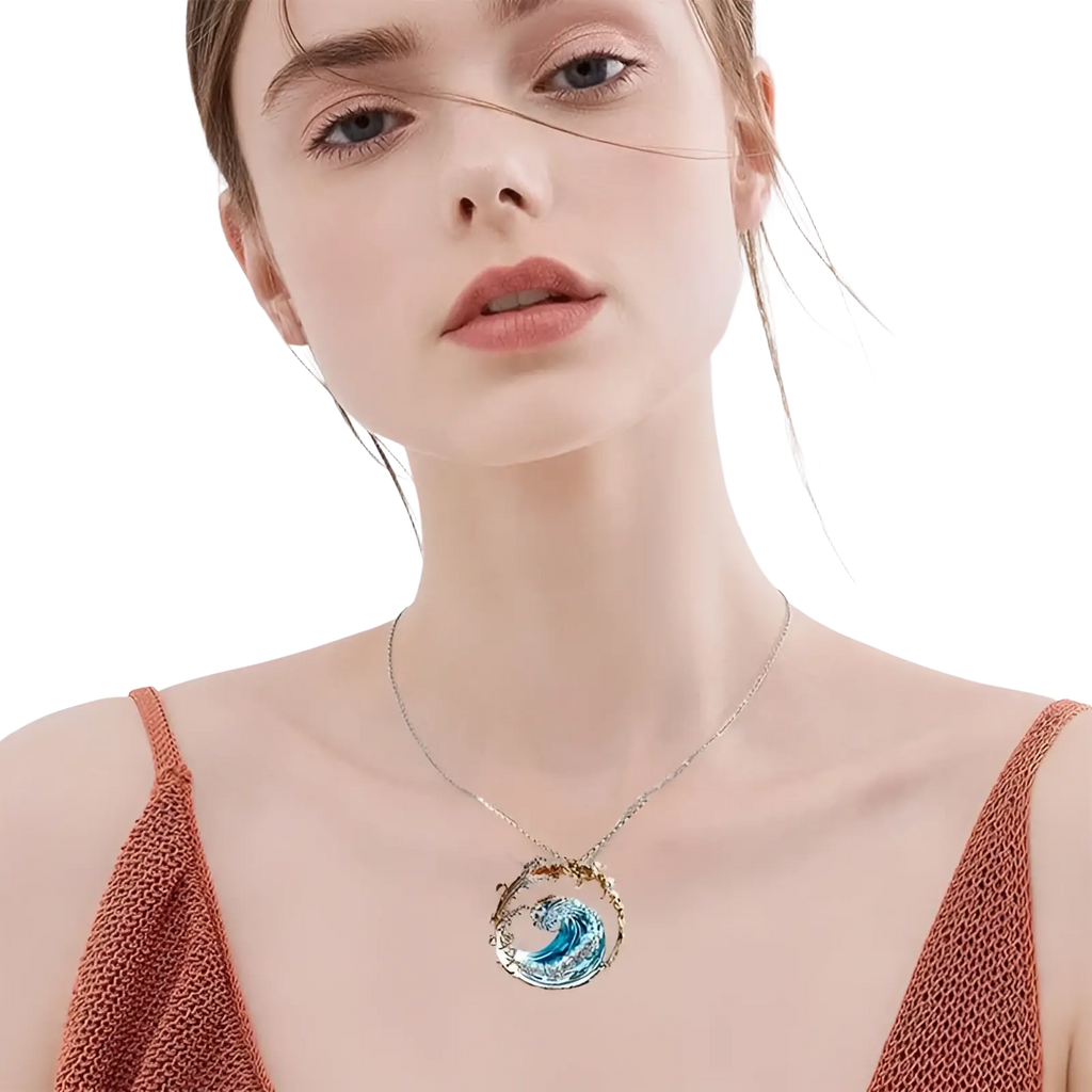 A delicate silver necklace with a circular turquoise glass pendant featuring an intricate blue wave design and gold accents