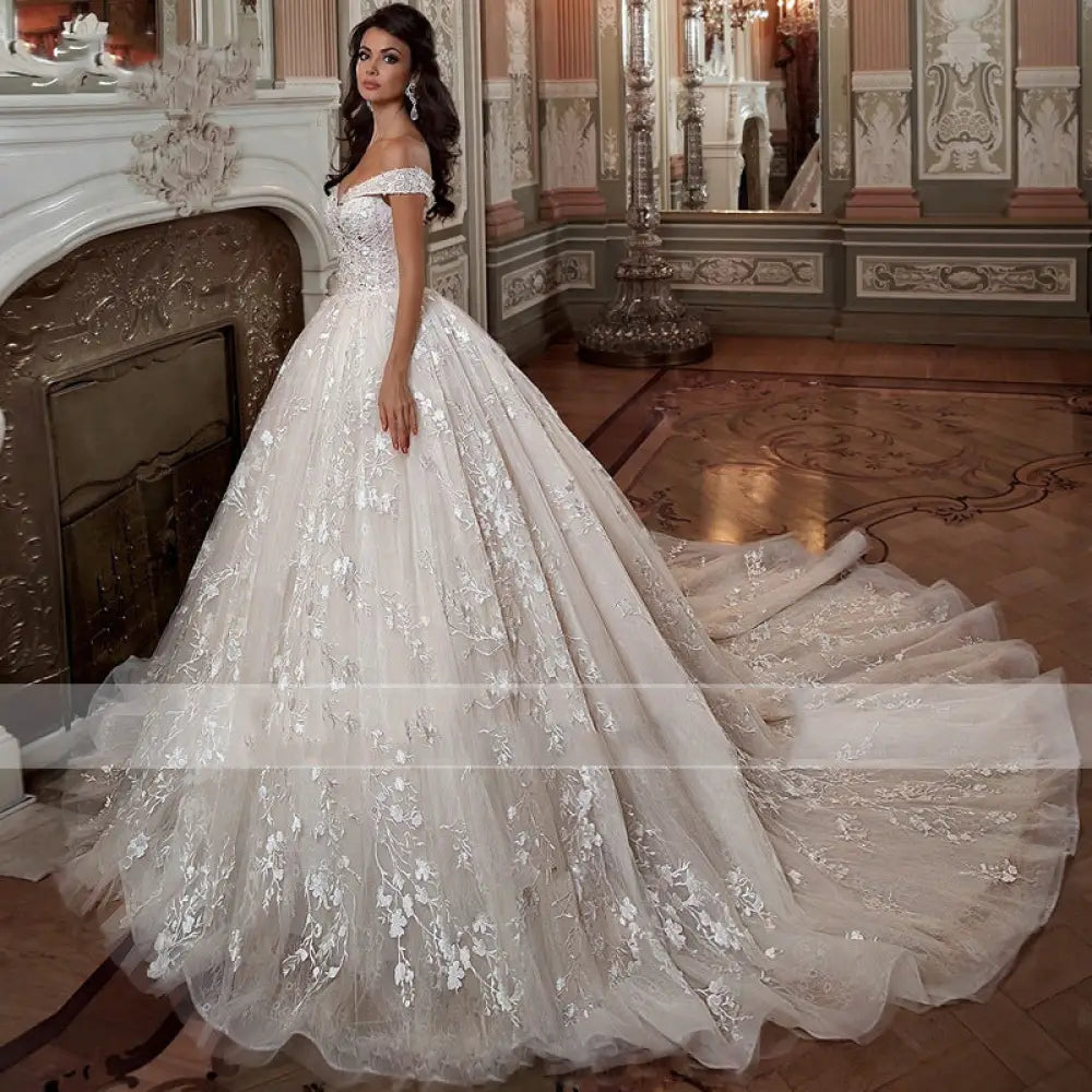 A voluminous ivory french mori off-shoulder wedding dress in lace with floral embroidery and a flowing tulle train
