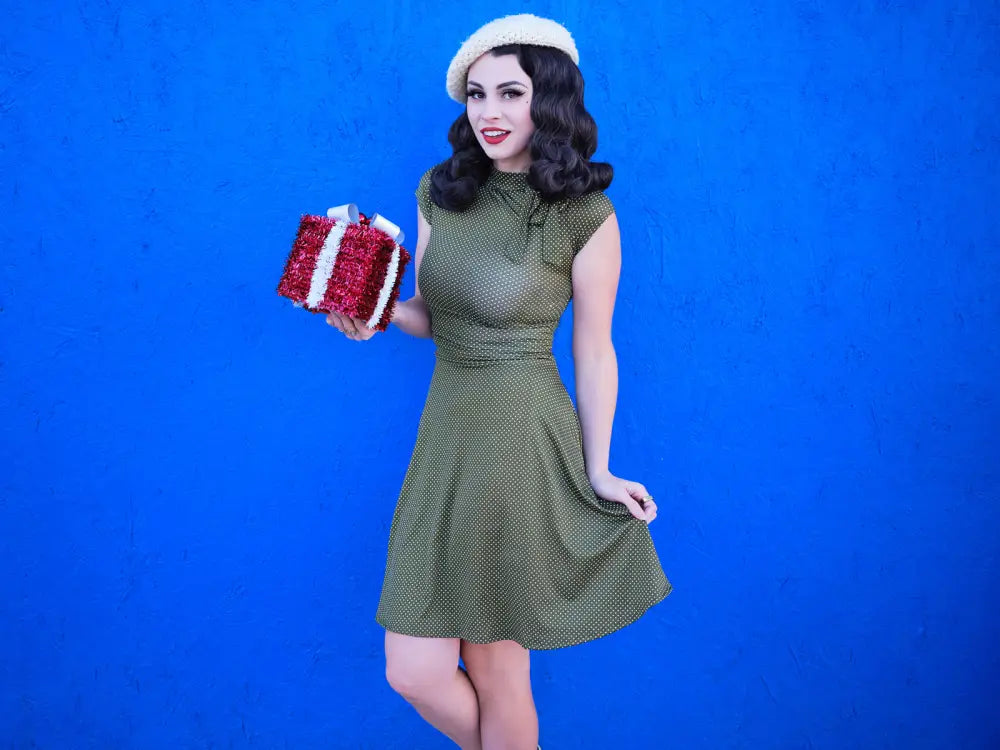 A festive red and white glittery gift box with a bow beside an olive dot bombshell retro plus size flare dress