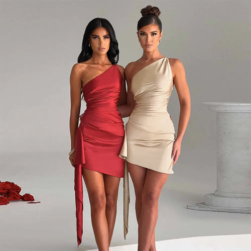 Two women wear beige satin ruched one shoulder backless mini dresses with draped side panels and asymmetrical hemlines
