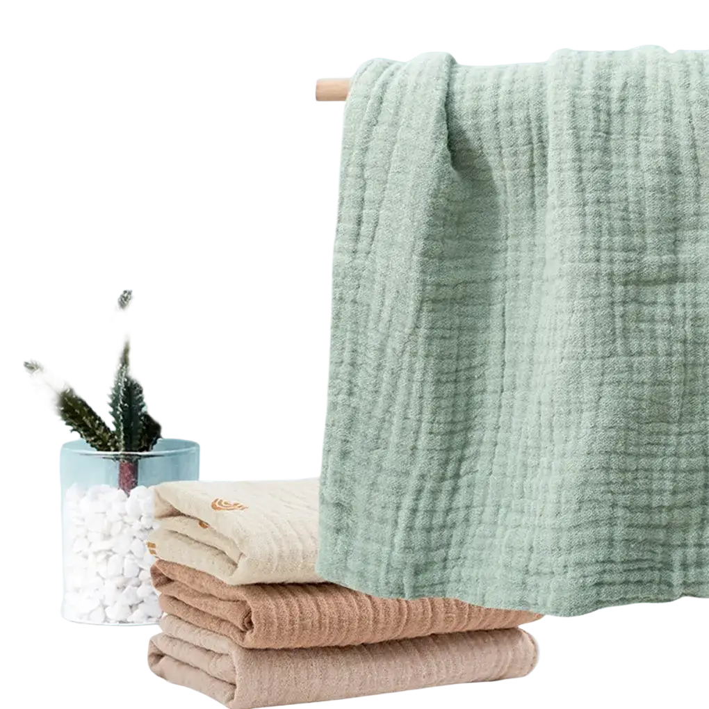 A soft light green organic cotton muslin baby bath towel with subtle grid texture hanging on a wooden rack