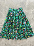 A vibrant green retro holiday pleated skirt with pockets featuring a festive pattern of colorful Christmas ornaments and pine branches