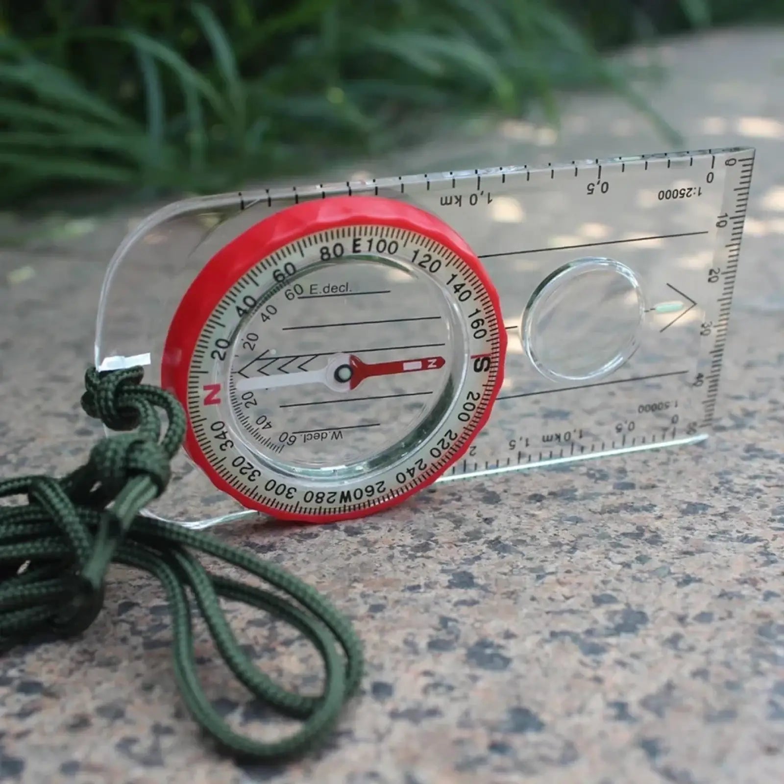 Outdoor navigation compass made of transparent plastic with red dial and green paracord lanyard for hiking
