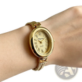 Gold-toned oval-faced quartz women watch with roman numerals and textured dial worn on wrist