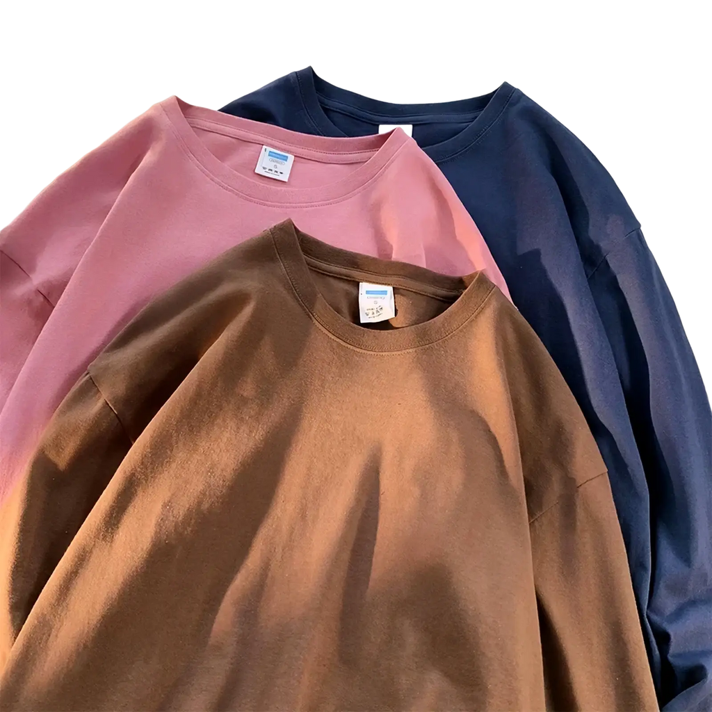 Three oversized crewneck long sleeve blank t-shirts in muted pink brown and navy blue on a white surface