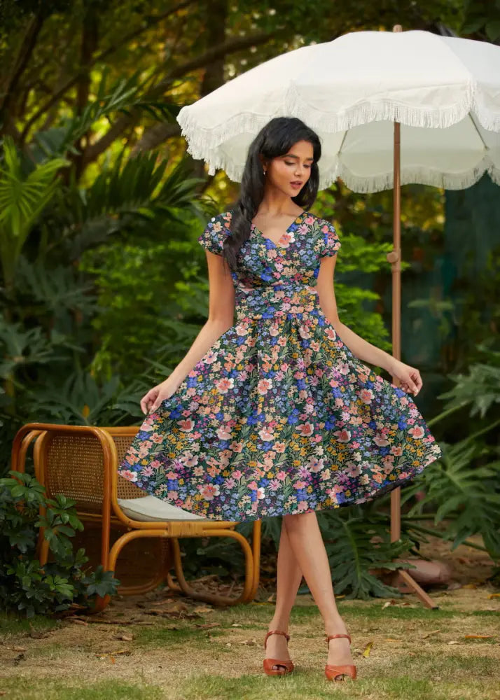 A woman wears a painted floral Greta cotton v neck midi dress with pockets featuring vibrant blossoms on navy