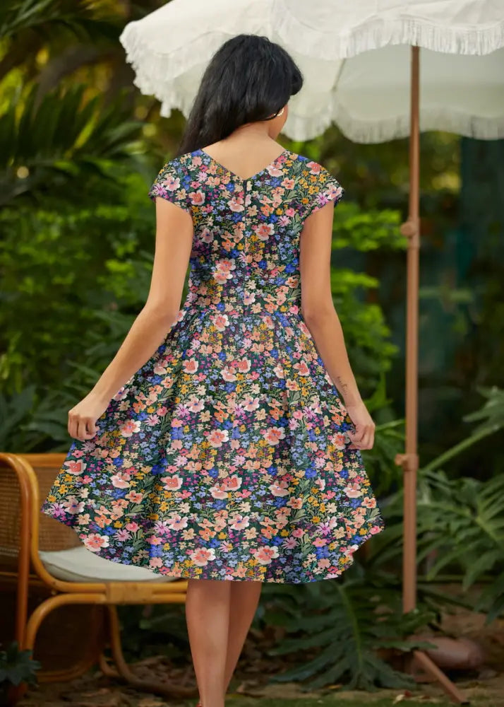A woman wearing a painted floral greta cotton v neck midi dress with pockets in vibrant blossoms on navy background