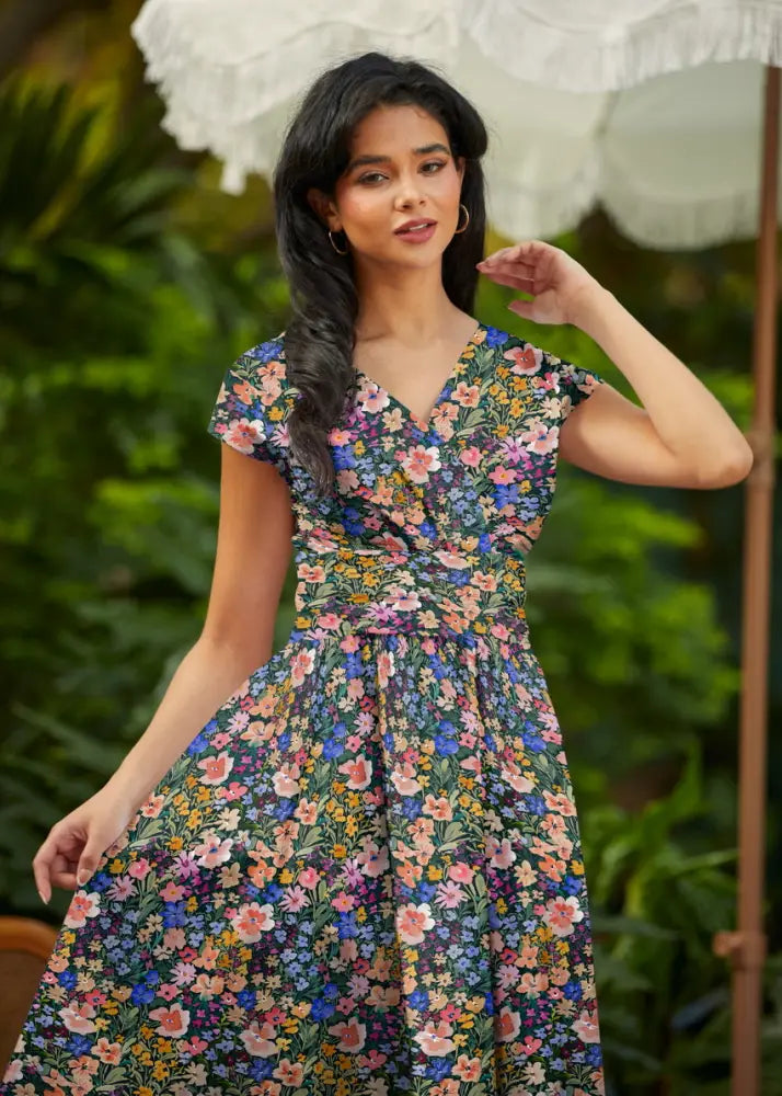 A woman wearing a dark green cotton painted floral Greta v neck midi dress with short sleeves and pockets