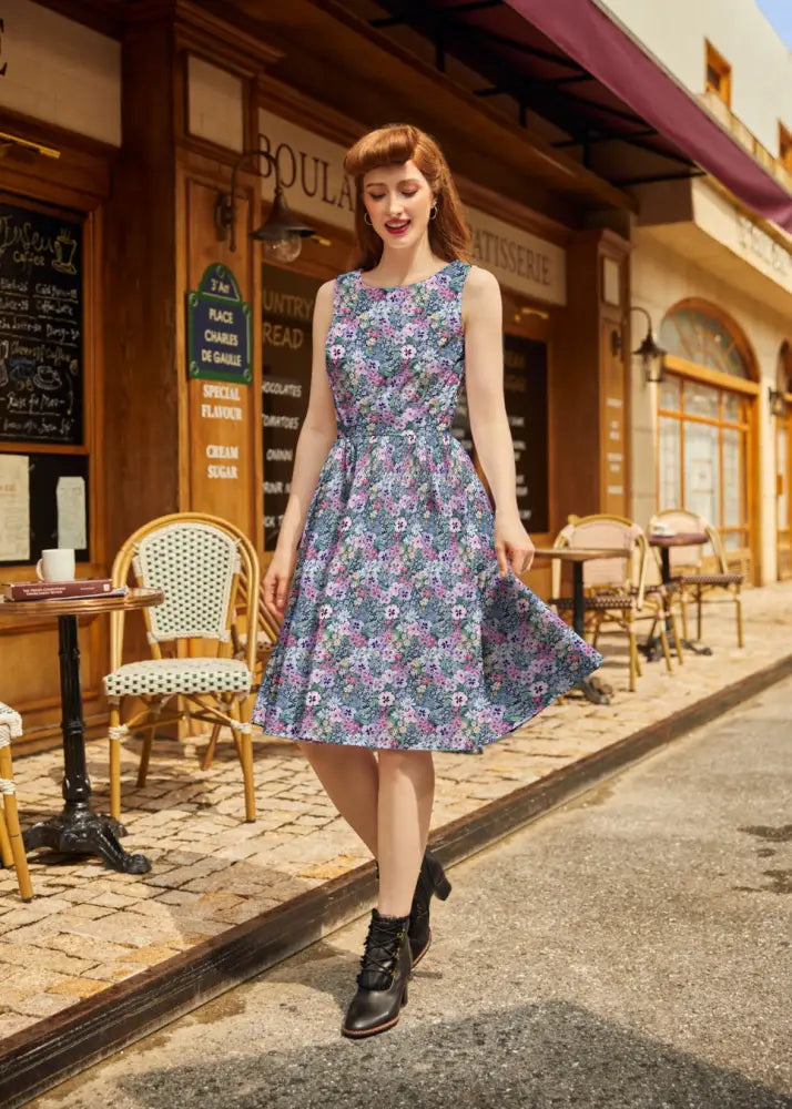 A vintage 1950s painted floral cotton sleeveless midi dress in soft blue and purple with fitted waist and flared skirt