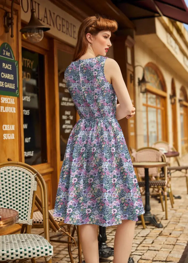 A woman wears a sleeveless 1950s painted floral cotton a-line midi dress with pockets in blue and pink shades