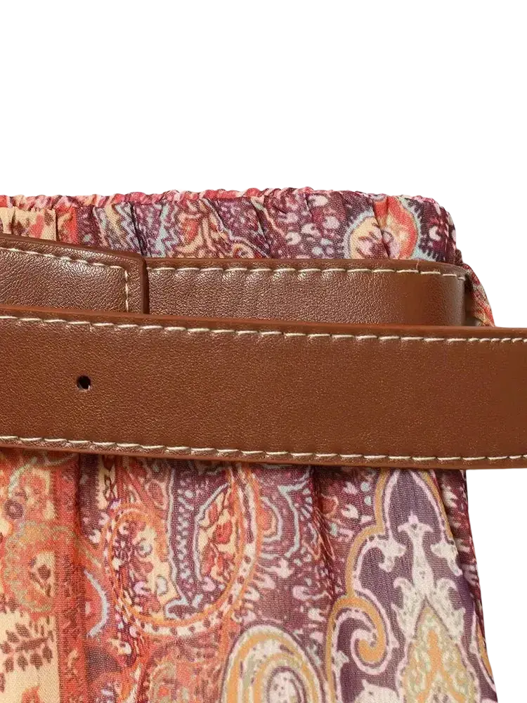 Brown leather strap with cream stitching attached to a fabric bag featuring intricate red purple and beige paisley print high waist midi design