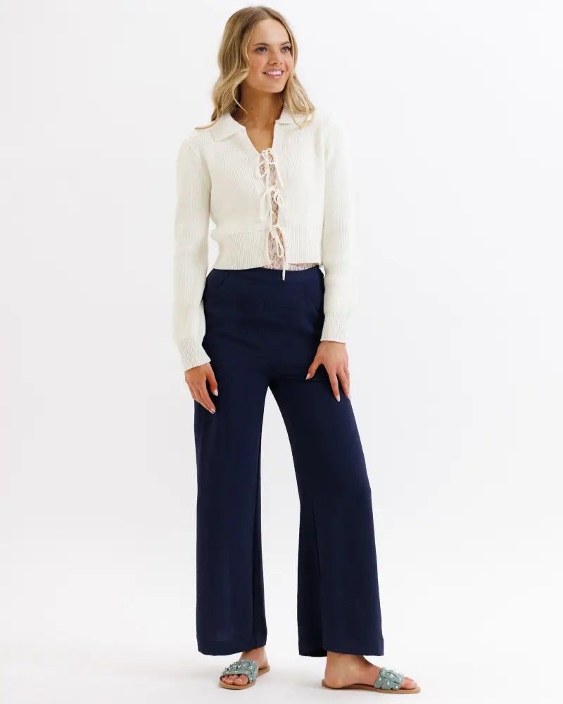 Cream-colored knit cardigan with lace-up front detail paired with parisian high waist navy wide leg pleated trousers