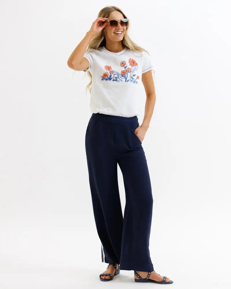 White short-sleeved t-shirt with embroidered orange and blue floral design paired with parisian high waist navy wide leg pleated trousers