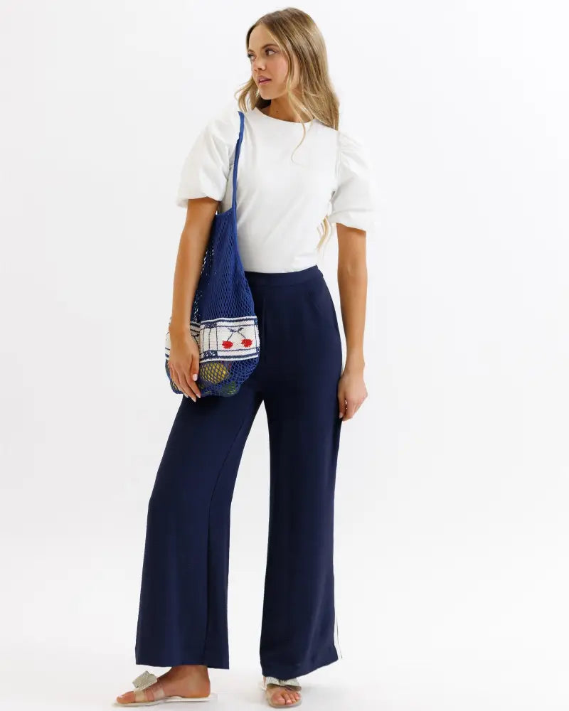 Blue woven mesh tote bag with embroidered cherry and green apple design paired with navy pleated trousers