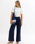 Blue woven mesh tote bag with embroidered cherry and green apple design paired with navy pleated trousers