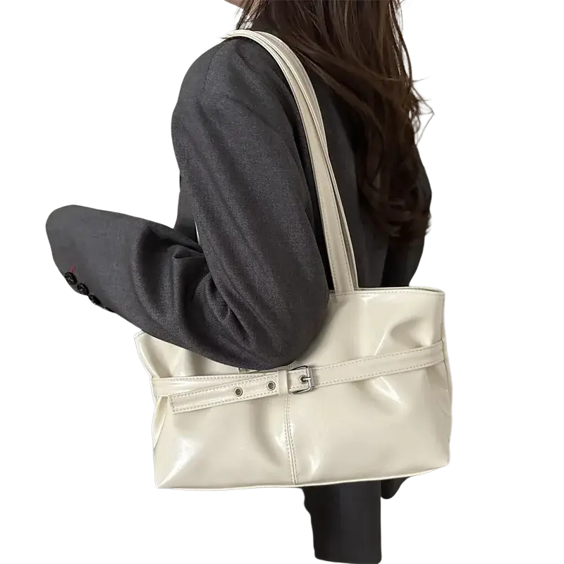 Cream-colored patent leather shoulder bag with adjustable shoulder strap and silver-toned buckle accent