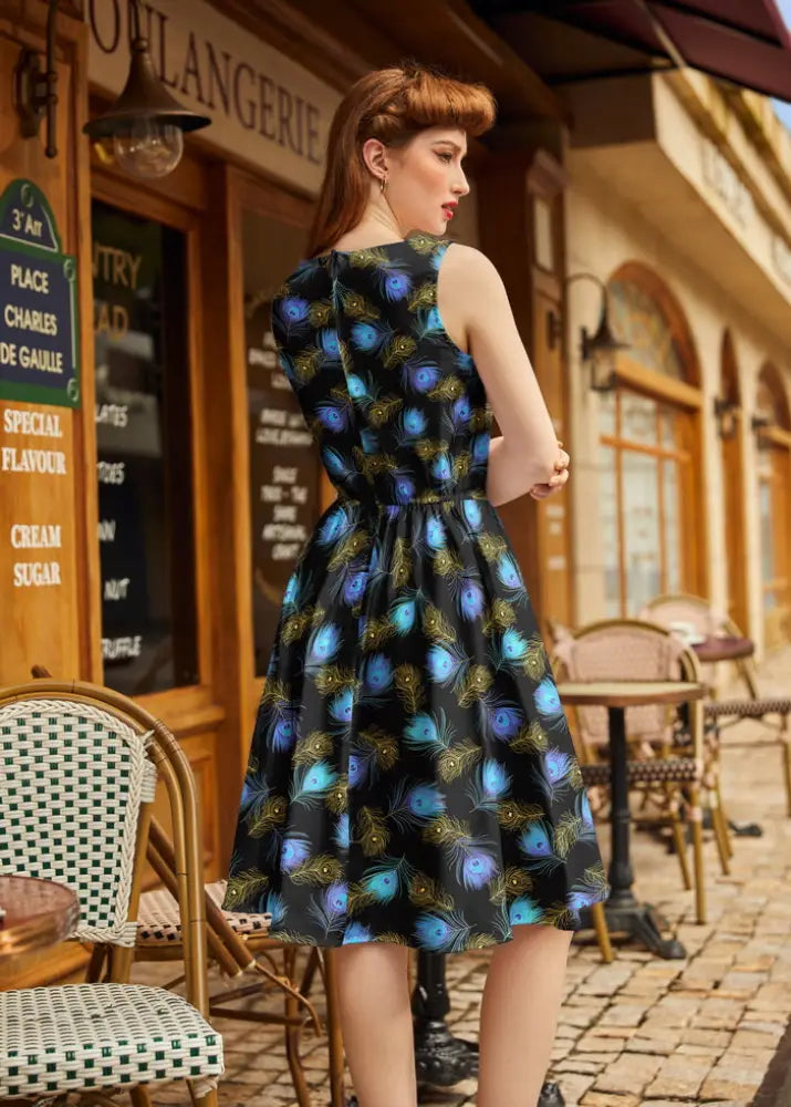 Black sleeveless cotton dress with vibrant blue and green peacock feather pattern, fitted bodice, and flared skirt