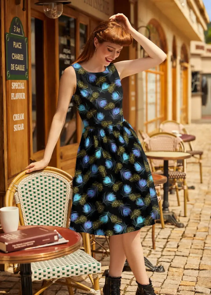 A vintage sleeveless black cotton dress with a fitted waist and vibrant blue and green peacock feather pattern