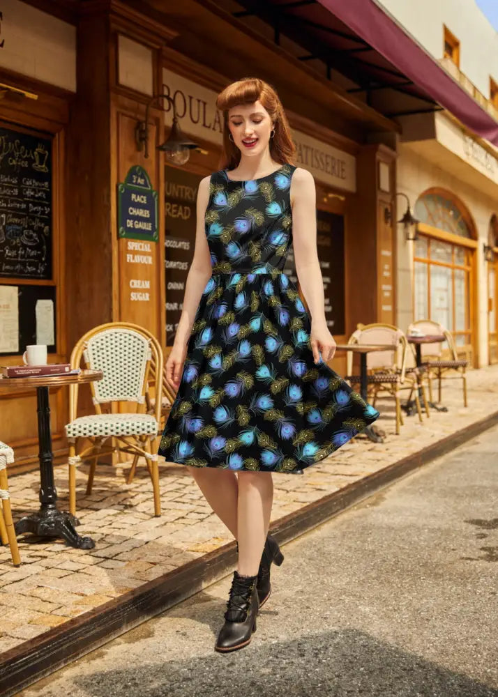 A black sleeveless vintage a-line cotton dress with a vibrant blue and green peacock feather pattern and fitted bodice