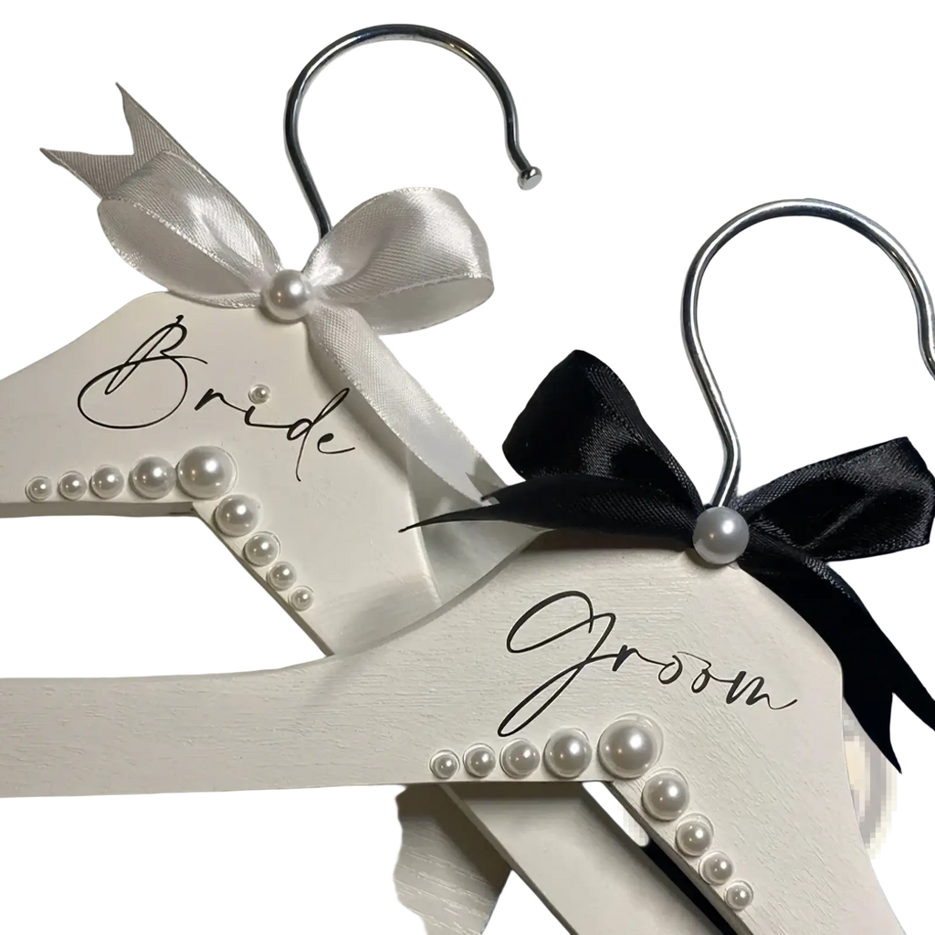 White wooden wedding hangers set with pearls satin bows one labeled bride in black cursive for bride and groom use