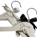 White wooden wedding hangers set with pearls satin bows one labeled bride in black cursive for bride and groom use