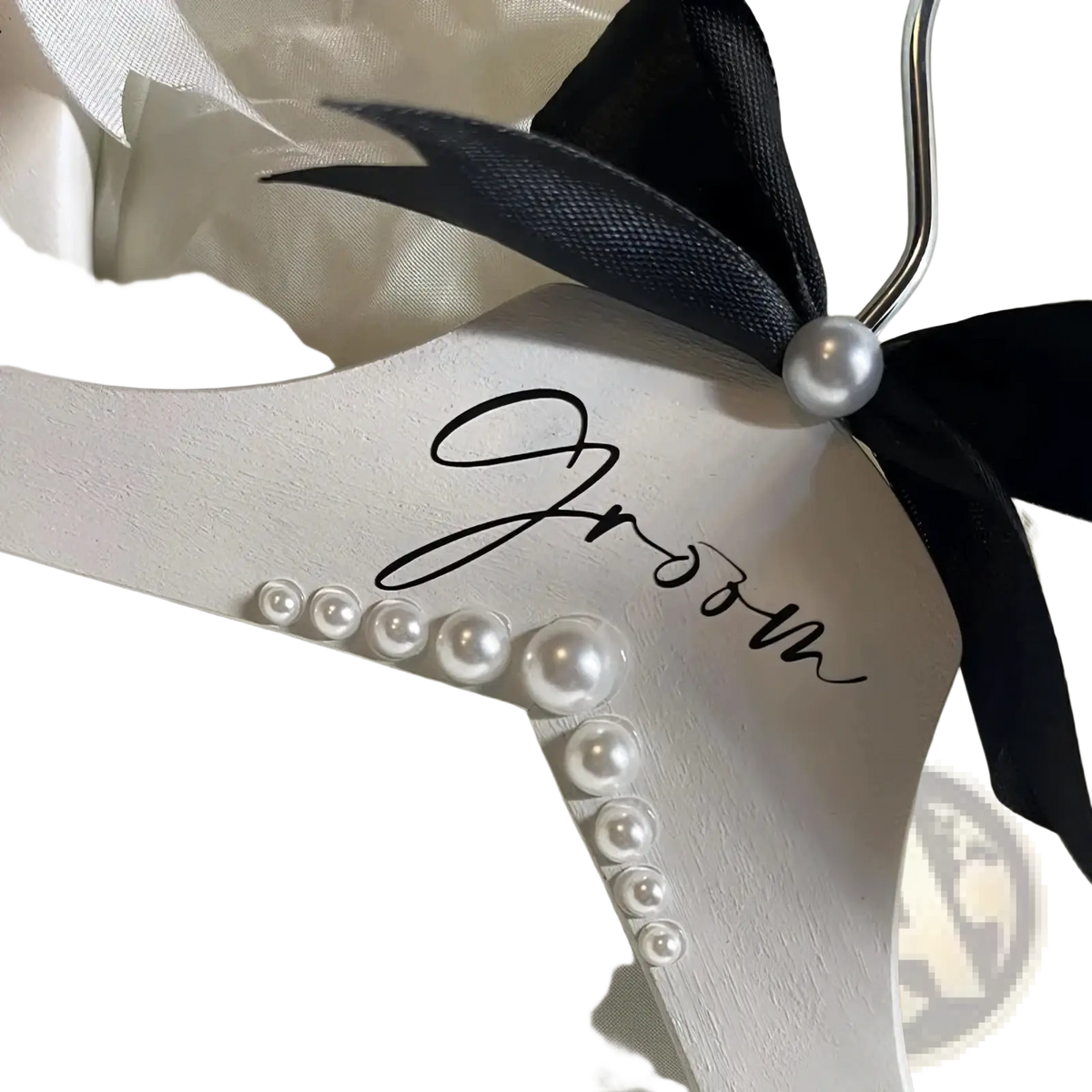 White wooden groom hanger with black ribbon bow, pearl accent, and cursive lettering adorned with graduated pearls